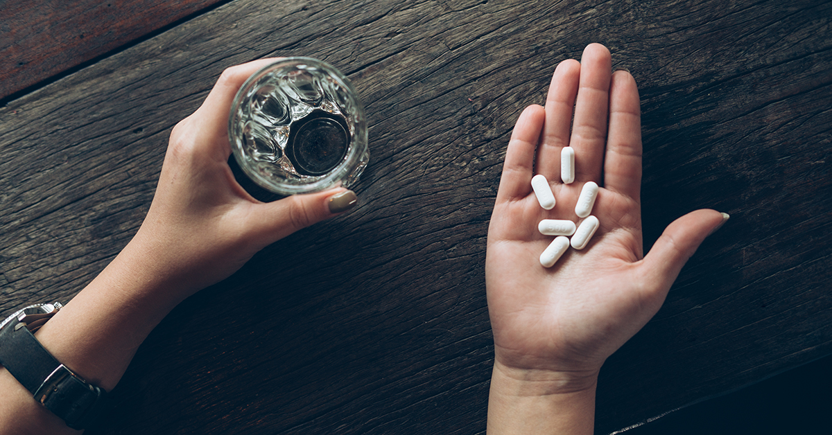 Pill of medicine in the hand with water on wooden background.