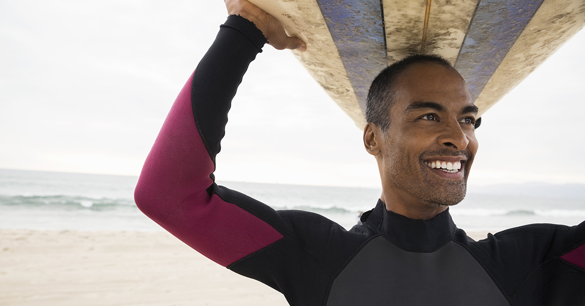 Smiling man in wetsuit holding surfboard overhead