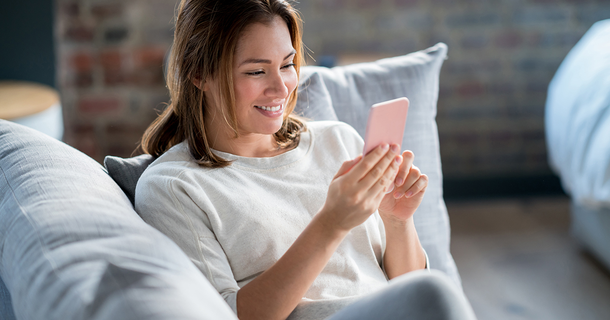 Beautiful woman relaxing at home using an app on her cell phone and looking happy - lifestyle concepts