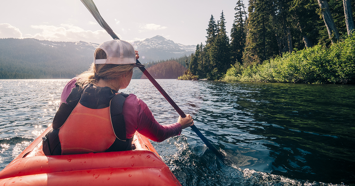 A woman paddles a kayak across a lake.