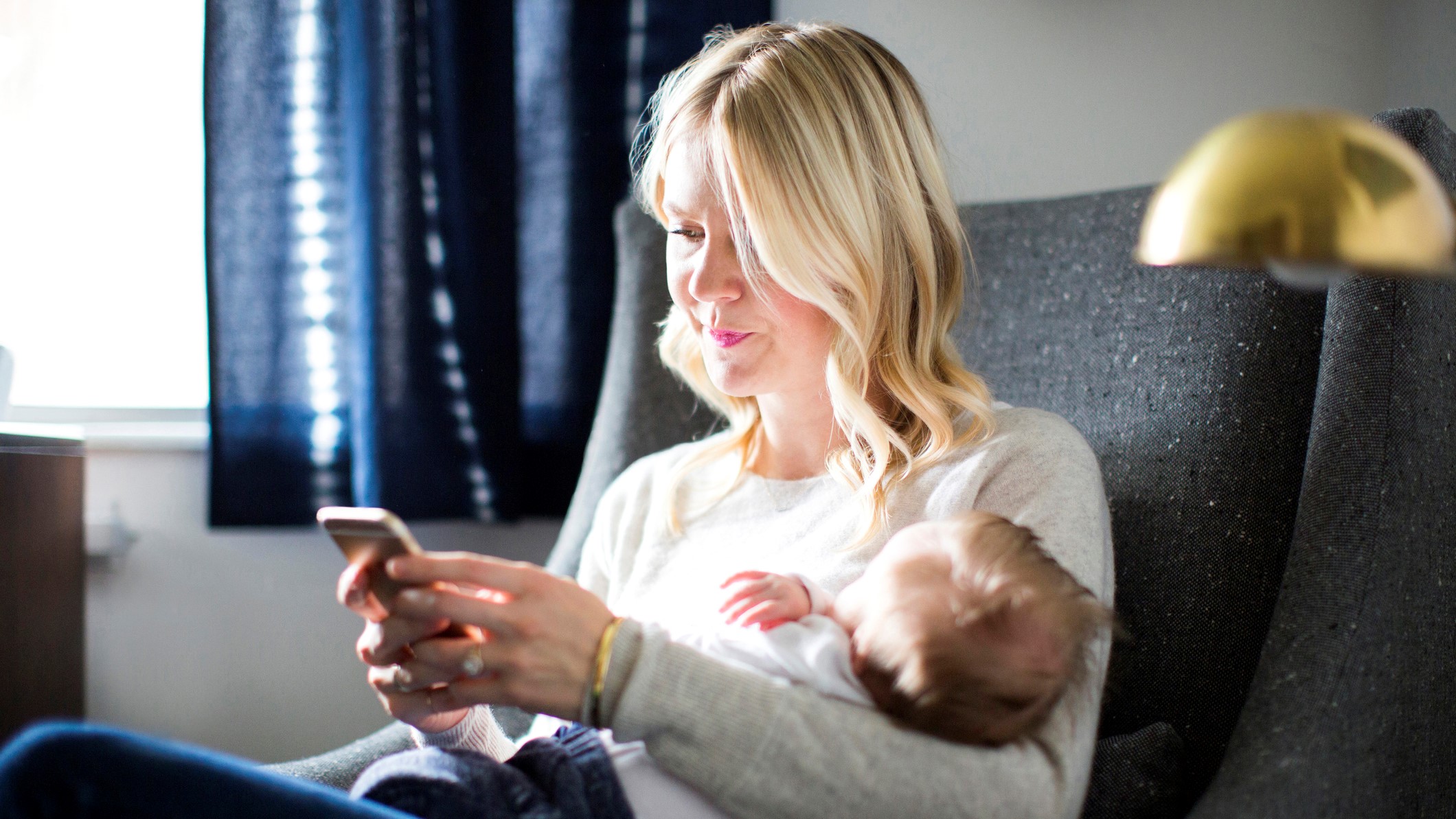 Woman holding her baby son while text messaging on smart phone.