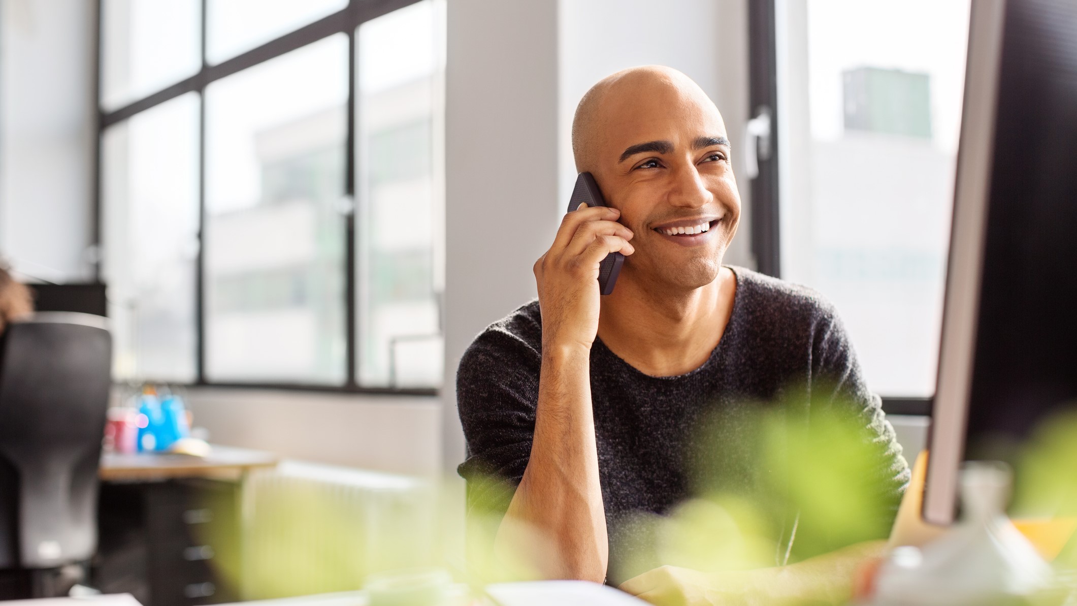 Mature man talking on phone and smiling. Hispanic male professional working at his desk in office.