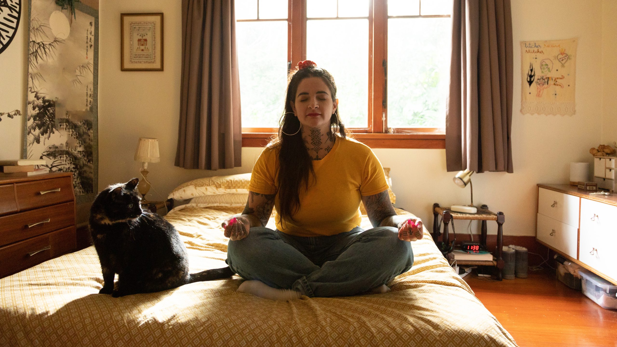 tattooed woman sitting on bed meditating with cat