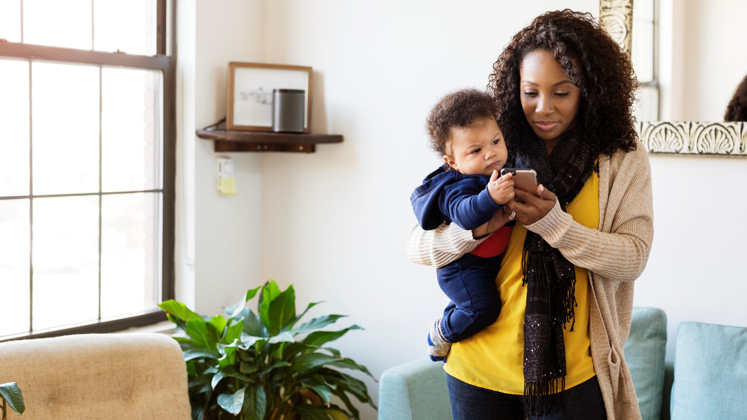 Woman with baby boy using mobile phone while standing at home