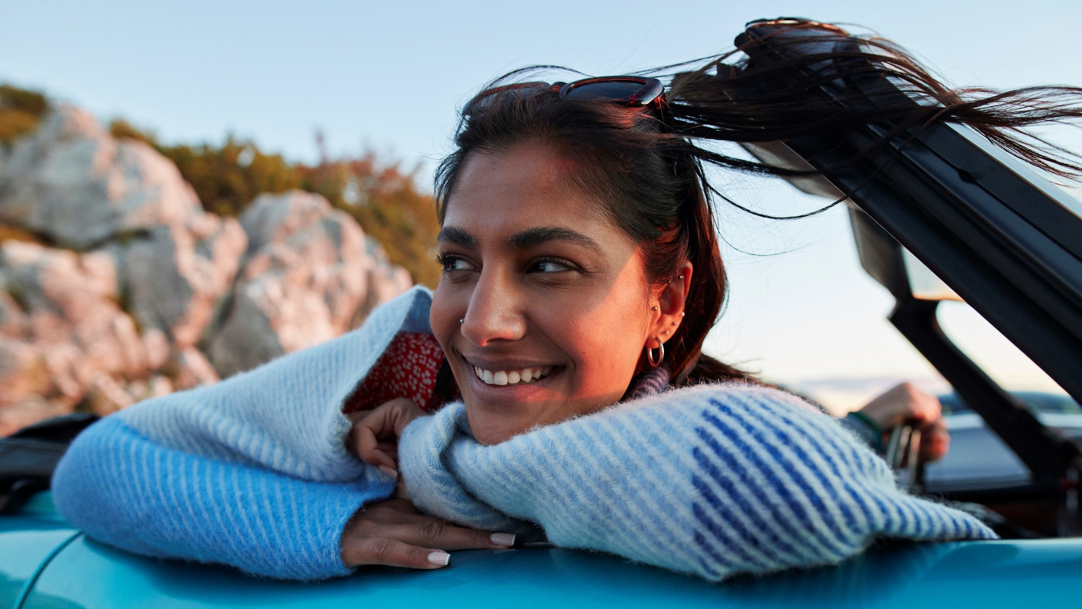 Smiling young woman day dreaming while leaning on convertible car during road trip