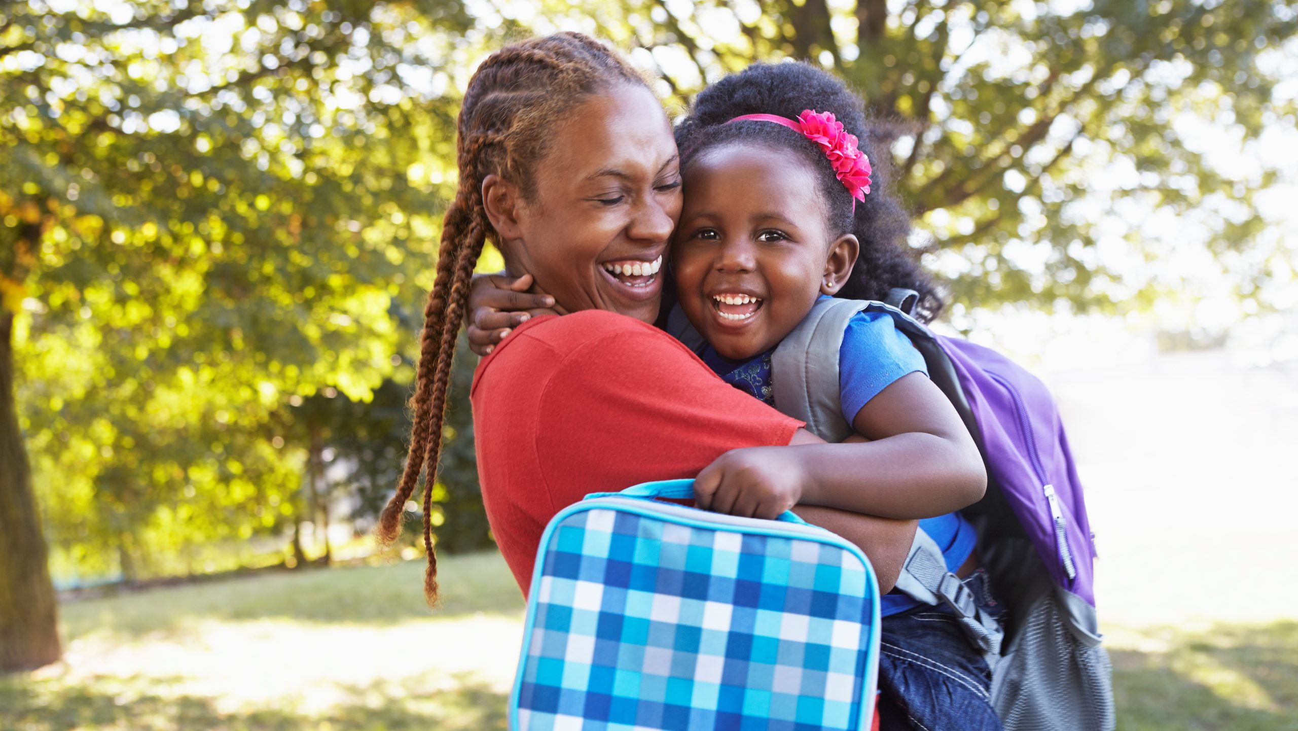 An image of a mother hugging daughter who is wearing a school backpack.