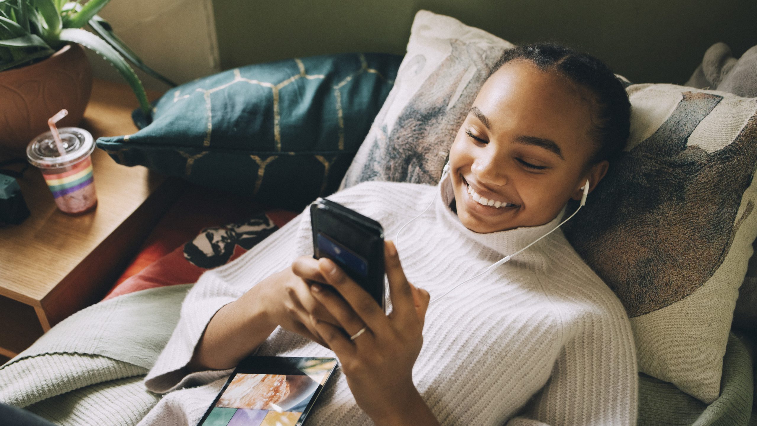An image of a smiling teen looking at a phone in bed.